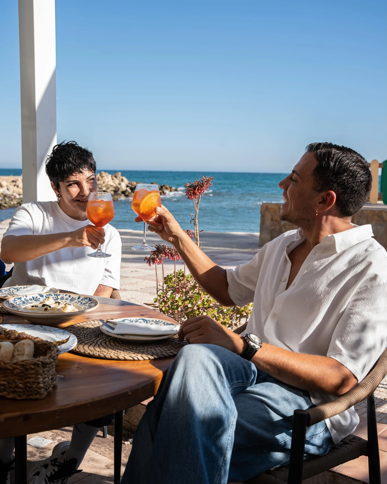 Pareja brindando con Aperol frente al mar al atardecer